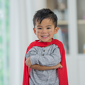 A young boy smiling in a superhero position